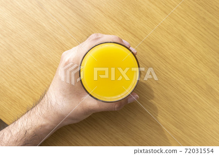 A man's hand holding a glass of orange juice 72031554