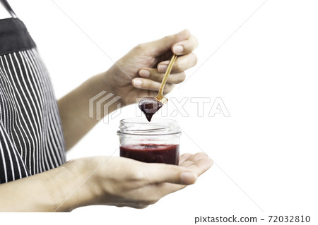 Woman hand holding a spoon with berry jam in jar in clipping path. 72032810