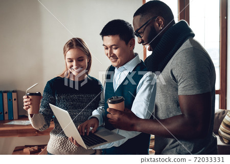 A woman stands near colleagues with cup of coffee. A woman stands near colleagues with cup of coffee. 72033331