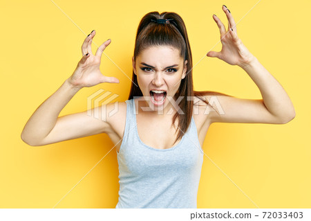Screaming emotional angry young woman close up portrait over yellow background 72033403