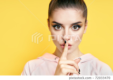 Close up portrait of pretty young woman keeps finger on lips, making hush gesture Close up portrait of pretty young woman keeps finger on lips, making hush gesture 72033470
