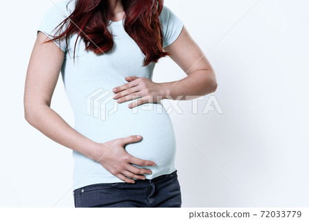 A girl with bloating is standing on a white.  72033779