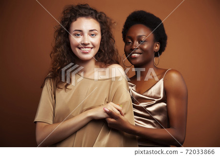 two pretty girls african and caucasian blond posing cheerful together on brown background, ethnicity diverse lifestyle people concept two pretty girls african and caucasian blond posing cheerful together on brown background, ethnicity diverse lifestyle people concept 72033866