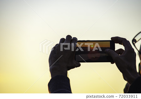 Hand holding the phone shooting the morning sun and the fog. Hand holding the phone shooting the morning sun and the fog. 72033911