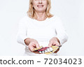 Woman shows pills to camera with outstretched hand 72034023