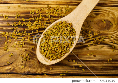 Fenugreek seeds in wooden spoon on wooden table 72034039