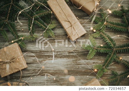 Gift boxes wrapped in craft paper, fir branches and garland lights. 72034657