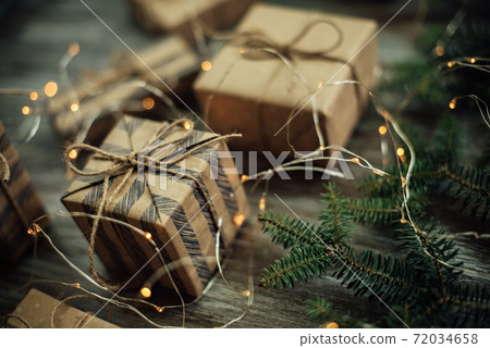 Gift boxes wrapped in craft paper, fir branches and garland lights. 72034658