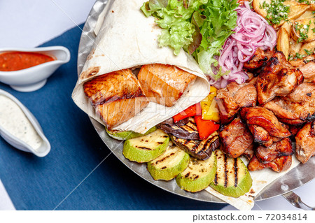 Mixed grill meat fried vegetables and grilled salmon fish fillets decoration in warm dish. Assorted delicious grilled kebab served with herbs on platter. Restaurant menu barbecue plate Bbq party meal 72034814