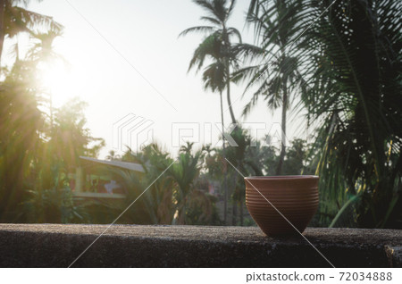 Coffee cup (Bhar) in sunset sunlight. Summer fresh cool look. Muddy mud tea cup made of clay for hot drink on roof beam of a residential building with bokeh city in the background. Coffee cup (Bhar) in sunset sunlight. Summer fresh cool look. Muddy mud tea cup made of clay for hot drink on roof beam of a residential building with bokeh city in the background. 72034888