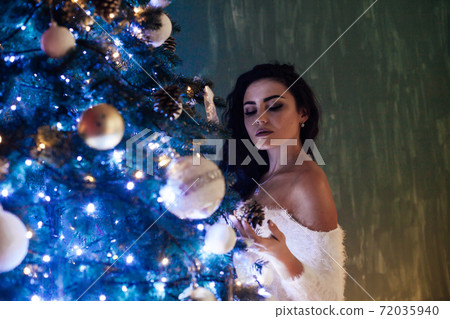Beautiful brunette woman decorates Christmas tree lights garland new year Beautiful brunette woman decorates Christmas tree lights garland new year 72035940