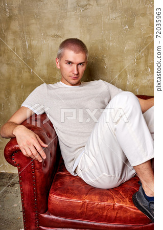 extraordinary confident young man in trendy wear posing on leather couch extraordinary confident young man in trendy wear posing on leather couch 72035963