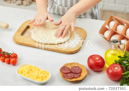 little child girl in cap and an apron knead the dough 72037301