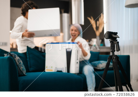 Happy videobloggers record unpacking video for their video blog with a brand new gaming console at home. Happy videobloggers record unpacking video for their video blog with a brand new gaming console at home. 72038626