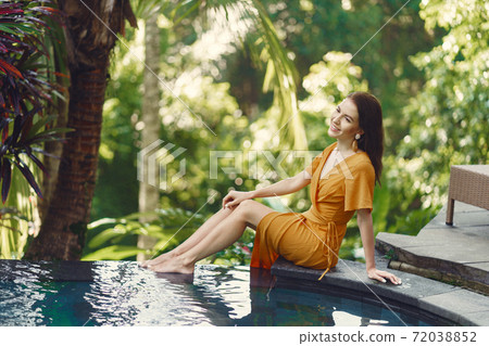 Woman in a yellow dress sitting by the pool in Bali Woman in a yellow dress sitting by the pool in Bali 72038852