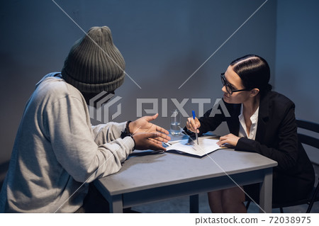 A black criminal in a hat communicates with his lawyer at the table in the police station A black criminal in a hat communicates with his lawyer at the table in the police station 72038975
