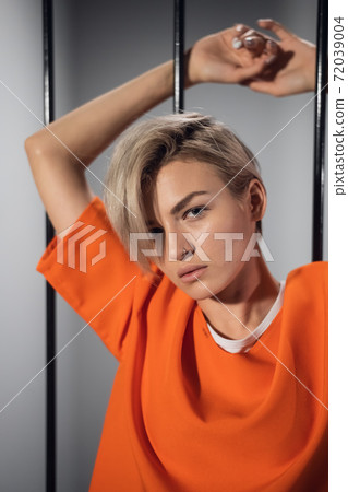 A close-up portrait of an orange-robed prisoner in prison against the background of prison bars 72039004