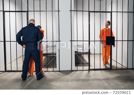 The guard has taken the prisoner out of the cell and is searching him. Another inmate watches from his cell. The guard has taken the prisoner out of the cell and is searching him. Another inmate watches from his cell. 72039021