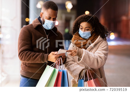 Portrait of black couple using phone wearing masks near mall Portrait of black couple using phone wearing masks near mall 72039519