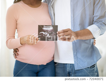 Cropped view of young pregnant couple holding photo of their unborn baby indoors, close up Cropped view of young pregnant couple holding photo of their unborn baby indoors, close up 72040071