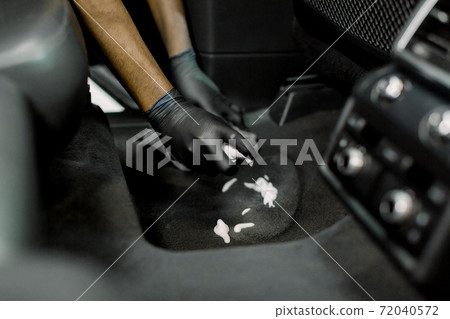 Cropped close up of hands of professional male detailer in black gloves, cleaning the carpet of car interior, applying disinfecting cleaning foam Cropped close up of hands of professional male detailer in black gloves, cleaning the carpet of car interior, applying disinfecting cleaning foam 72040572