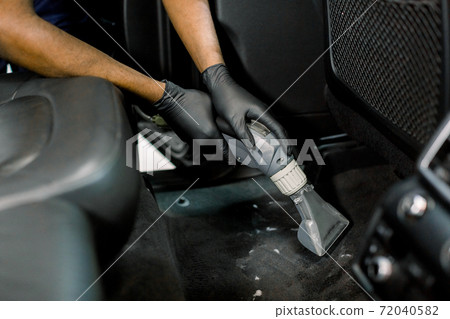 Cropped close up shot of hands of African male worker at auto service station, using vacuum cleaner in car, remowing the dust and sand. Vacuum cleaning inside the car Cropped close up shot of hands of African male worker at auto service station, using vacuum cleaner in car, remowing the dust and sand. Vacuum cleaning inside the car 72040582