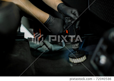 Close up cropped image of male hands in protective gloves, cleaning car interior and floor by chemical foam and scrubbing machine, electric brush. Car detailing and wash concept Close up cropped image of male hands in protective gloves, cleaning car interior and floor by chemical foam and scrubbing machine, electric brush. Car detailing and wash concept 72040586