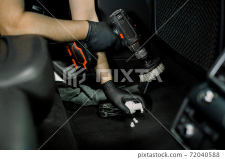 Cropped close up image of male hands, worker of auto service station, cleaning car floor and interior with disinfecting foam and electric brush cleaner. Car detailing concept 72040588