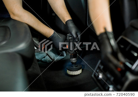 Cropped image of auto service staff, two workers in gloves, cleaning car interior with soft and electric brushes, removing the dust from plastic panel and floor. Detailing and valeting concept Cropped image of auto service staff, two workers in gloves, cleaning car interior with soft and electric brushes, removing the dust from plastic panel and floor. Detailing and valeting concept 72040590