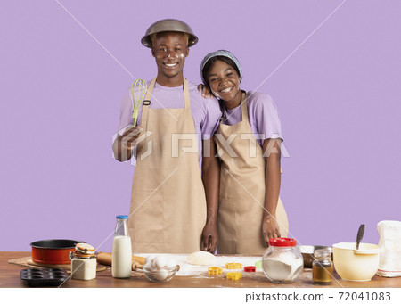 Portrait of happy black couple with dirty faces cooking together on violet studio background 72041083