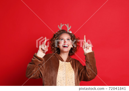 Funny female in reindeer costume smiling and pointing up Funny female in reindeer costume smiling and pointing up 72041841
