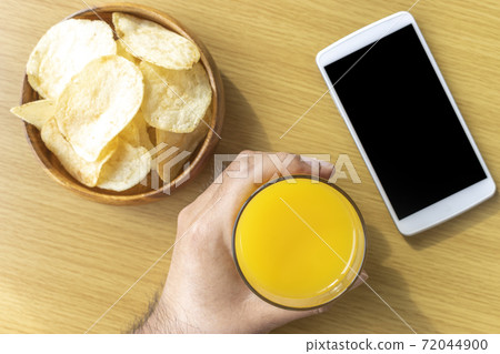 The hand of a man who eats a snack during a break and operates a smartphone The hand of a man who eats a snack during a break and operates a smartphone 72044900