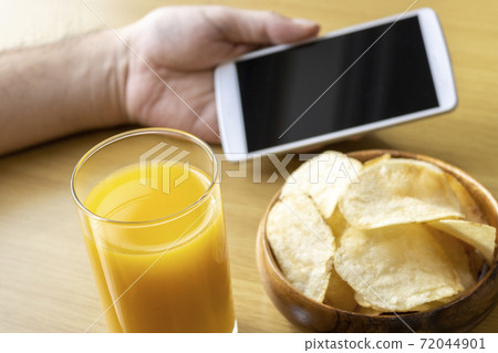 The hand of a man who eats a snack during a break and operates a smartphone The hand of a man who eats a snack during a break and operates a smartphone 72044901