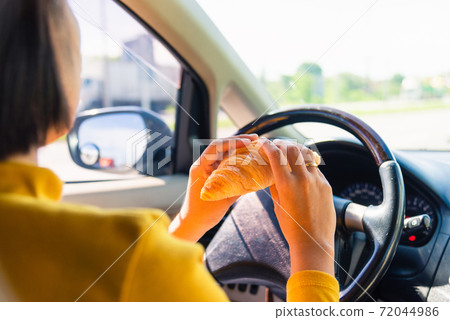woman eating food fastfood while driving the car woman eating food fastfood while driving the car 72044986