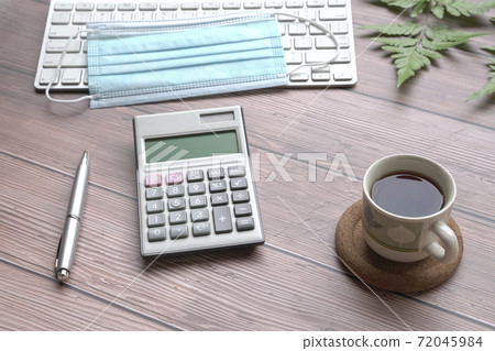 Wood table with keyboard, face mask, coffee, pen, calculator and green plants. Wood table with keyboard, face mask, coffee, pen, calculator and green plants. 72045984