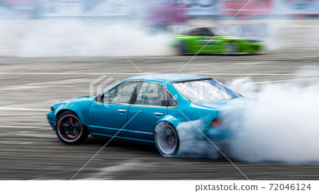 Blurred car drifting, Two car drifting battle on asphalt street road race track, Automobile and automotive drift car with smoke from burning tire on speed track. 72046124