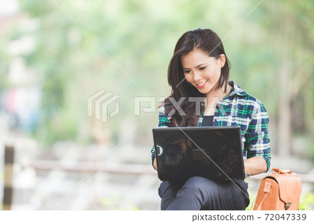 Young asian woman using laptop while sitting on the park Young asian woman using laptop while sitting on the park 72047339