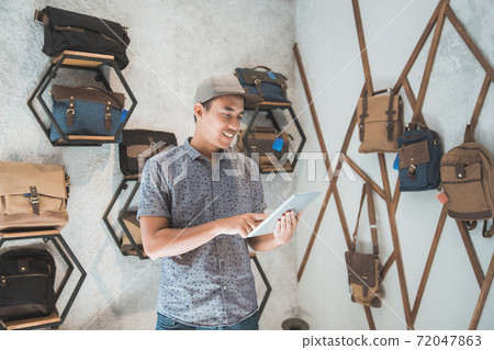 asian male business owner in a bag shop with tablet asian male business owner in a bag shop with tablet 72047863