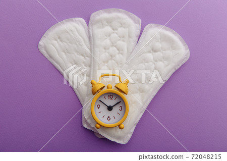Menstrual pads and yellow alarm clock on lilac background. Female's menstrual cycle concept Menstrual pads and yellow alarm clock on lilac background. Female's menstrual cycle concept 72048215