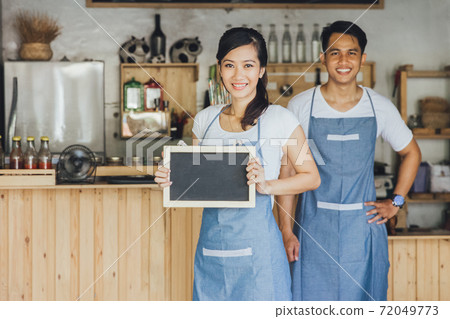 young female waitress standing and holding blank blackboard sign at a cafe young female waitress standing and holding blank blackboard sign at a cafe 72049773