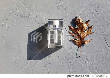 Rectangular transparent glass perfume bottle and golden leaf on gray textured background. Top view, trendy shadow and copy space. Rectangular transparent glass perfume bottle and golden leaf on gray textured background. Top view, trendy shadow and copy space. 72050097