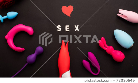 The inscription sex heart and a collection of multicolored vibrators on a black background. Sex toys of various shapes. Assortment of sex shop The inscription sex heart and a collection of multicolored vibrators on a black background. Sex toys of various shapes. Assortment of sex shop 72050649