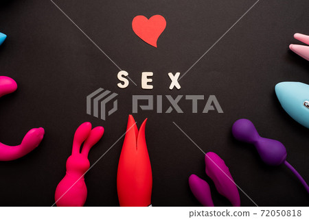 The inscription sex heart and a collection of multicolored vibrators on a black background. Sex toys of various shapes. Assortment of sex shop The inscription sex heart and a collection of multicolored vibrators on a black background. Sex toys of various shapes. Assortment of sex shop 72050818