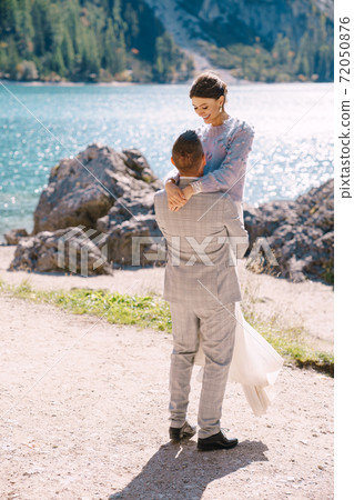 Bride and groom under an autumn tree, with fiery yellow foliage, at the Lago di Braies in Italy. Destination wedding in Europe, on Braies lake. The newlyweds in love are dancing and spinning. 72050876