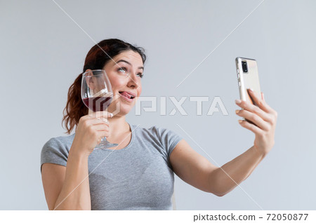 Caucasian woman drinks red wine and communicates with friends via video communication on a smartphone. The quarantined girl celebrates the holiday via an online conference 72050877