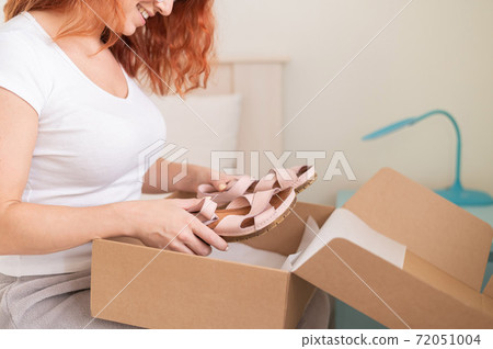 Happy woman unpacks online shopping for shoes. The girl received the package and opens it while sitting in the bedroom Happy woman unpacks online shopping for shoes. The girl received the package and opens it while sitting in the bedroom 72051004
