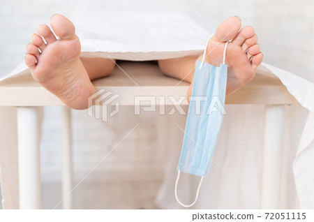 Close-up of dead men feet in a morgue with a medical mask on a toe. An unrecognizable woman has died from the coronavirus 72051115