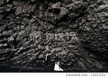 Destination Iceland wedding. Wedding couple under a rock of basalt stones. Bride and groom on the black beach of Vik. 72051281