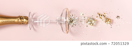 Bottle of champagne, glass with splash of confetti and golden decorations over pink background 72051329