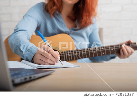 A woman with a guitar writes notes in a notebook. The girl composes a song 72051387